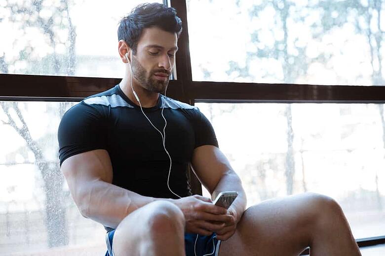 Athletic man wearing black t-shirt listening to music sitting on windowcill