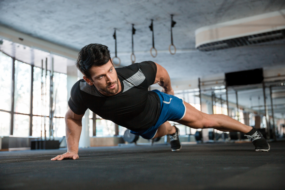 Uomo che fa esercizio di flessioni con una mano in palestra