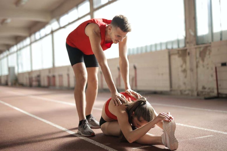 Personal Trainer CONI che aiuta ragazza a fare stretching su campo di atletica